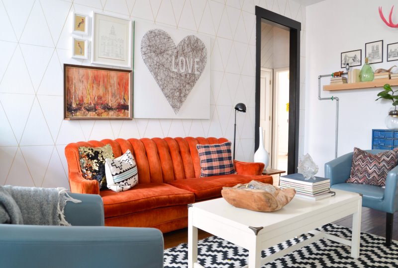 Oranžinė sofa gyvenamajame kambaryje su baltomis sienomis