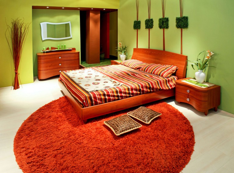 Oranžinė lova ir kilimas miegamojo interjere
