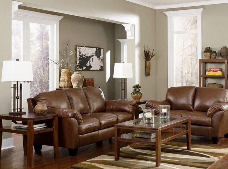 Brūns mākslīgās ādas dīvāns pret gaiši pelēkām viesistabas sienām