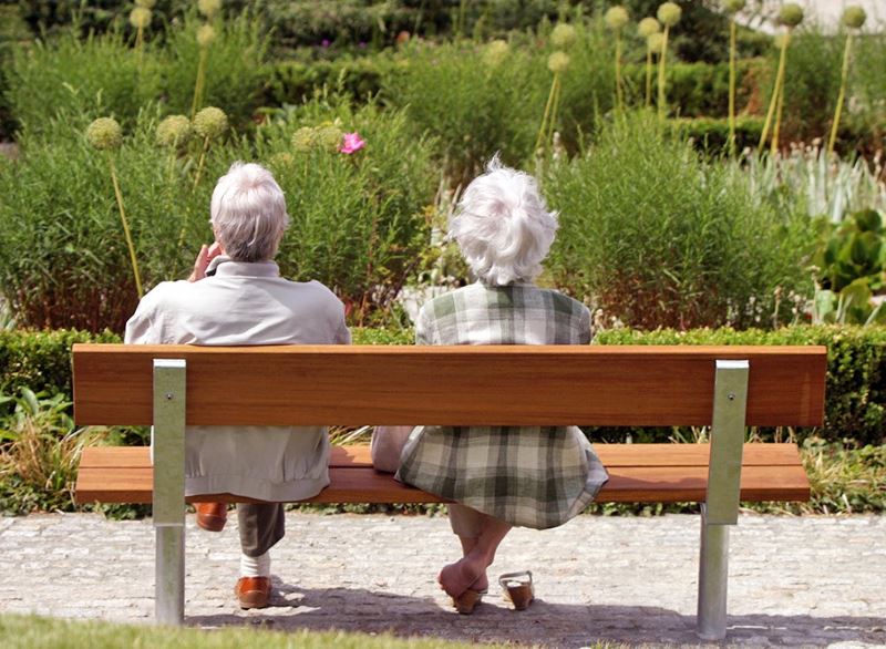 Възрастните хора се отпускат на дървена пейка в парк за отдих