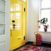 Priekštelpā dzelteno durvju priekšā krāsains paklājs