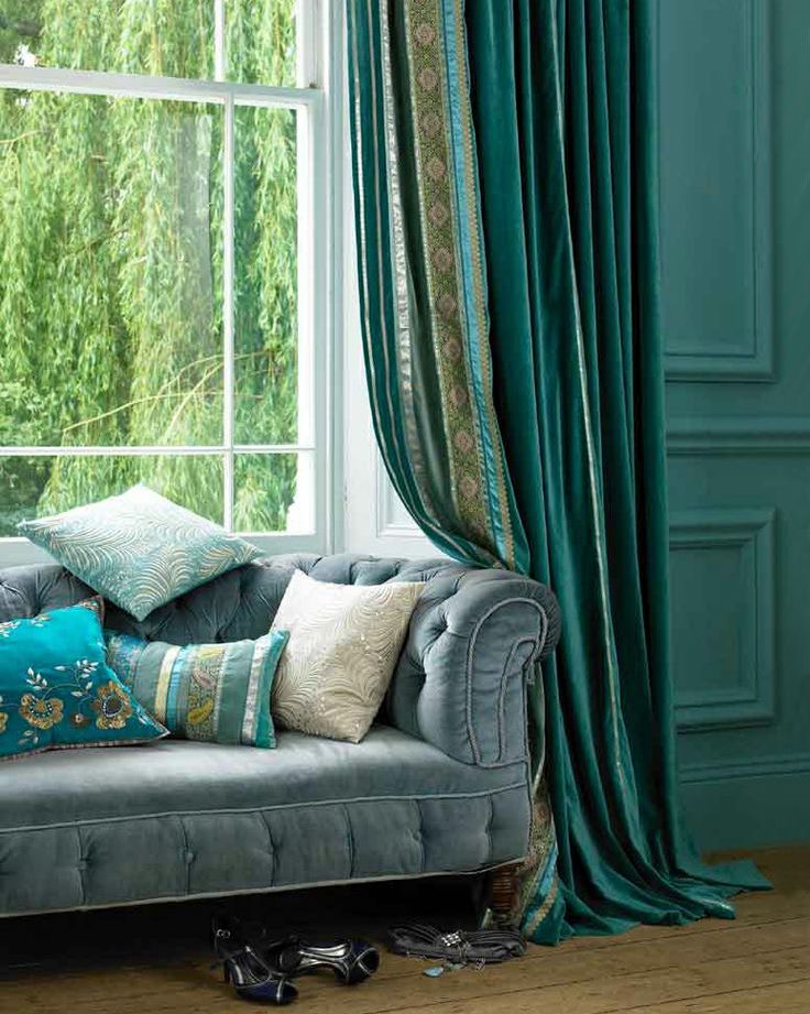 Sofa priešais svetainės langą su smaragdinėmis užuolaidomis