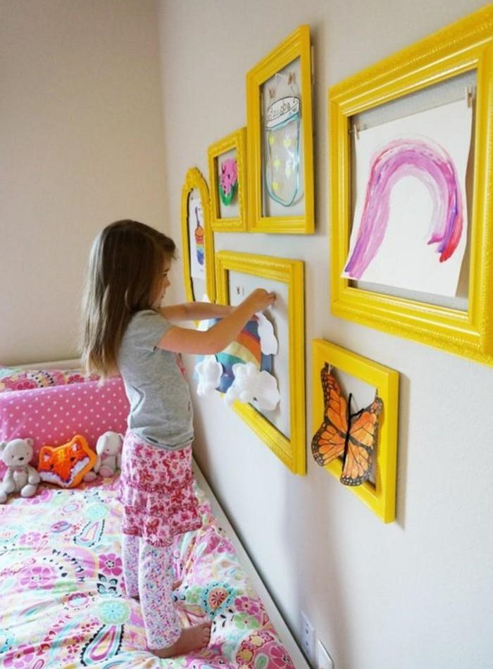 Dívka zdobí místnost svými vlastními kresbami.
