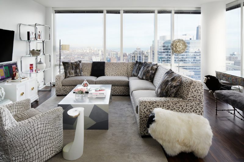 Pohovka s šedými a béžovými polštáři v obývacím pokoji s velkými okny