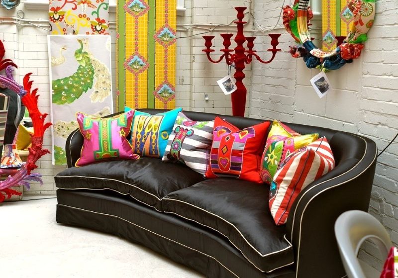 Ryškios pagalvės, rėkiančios spalvos ant tamsiai rudos sofos